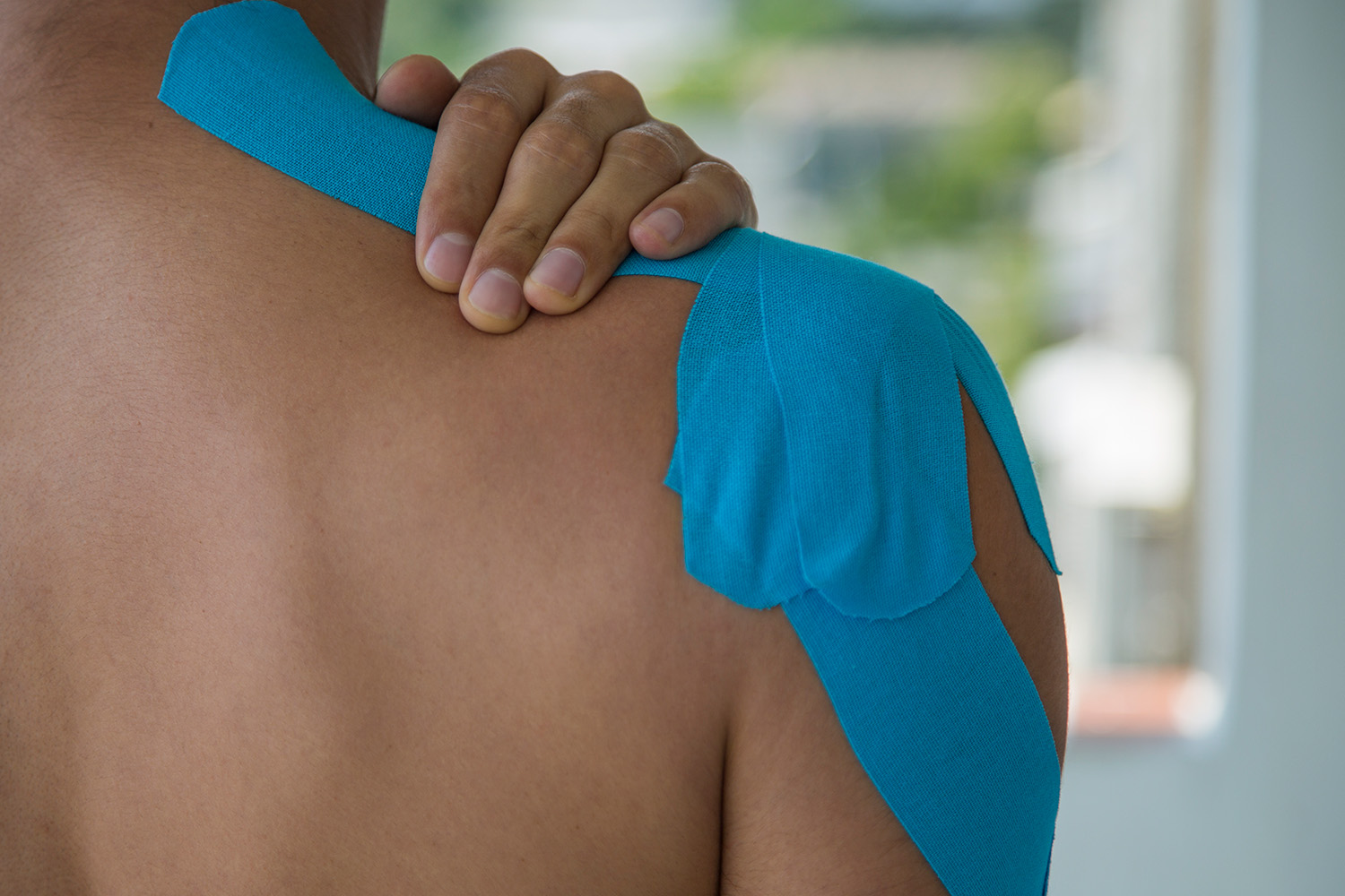 A person with kinesiology tape on their shoulder, holding the joint in pain, representing shoulder pain symptoms treated by chiropractors in Overland Park.